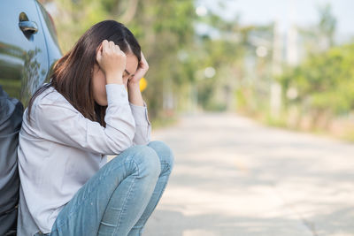 Tensed woman with head in hands crouching against car