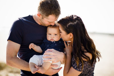 Mother & father kiss infant son on beach