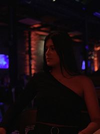 Young woman looking away while standing at illuminated restaurant