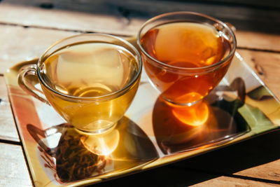 Prepared hot herbal, red, yellow and black tea shining on the sunset sun in two transparent cups 