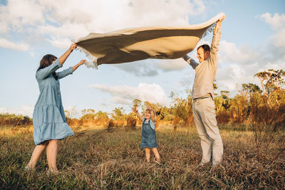 Young couple with cute 2 years old daughter under waving blanket