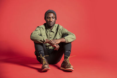 Portrait of young man sitting against red background