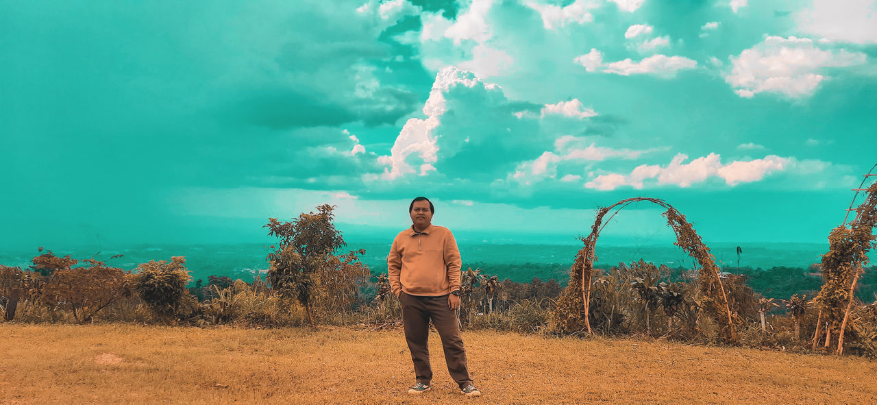 REAR VIEW OF MAN STANDING ON FIELD