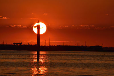 Silhouette built structure by sea against orange sky