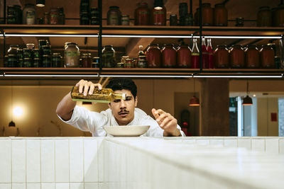 Focused male chef pouring ingredient in bowl at commercial kitchen in restaurant