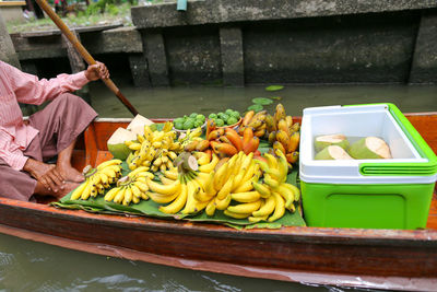 Low section of man with fruits sitting no boat in lake