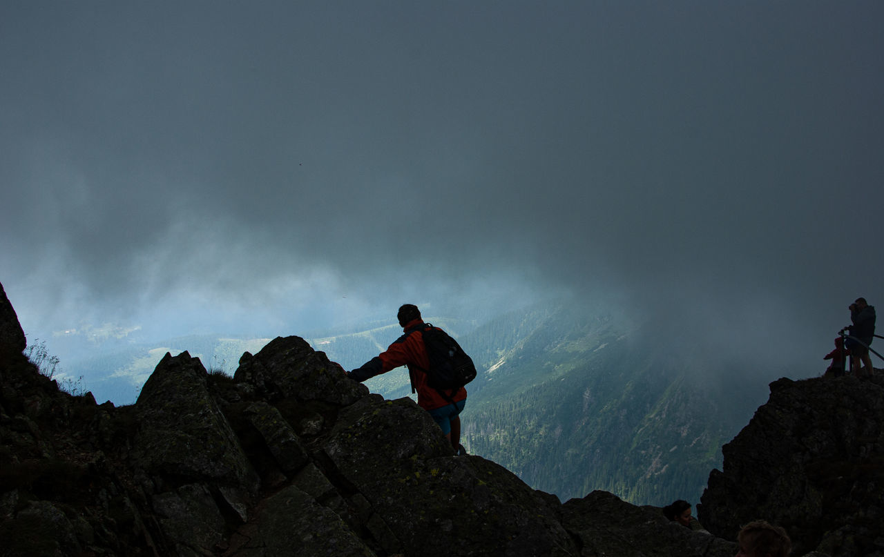 PEOPLE STANDING ON ROCKS AGAINST MOUNTAIN RANGE