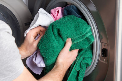 Cropped hand of man putting clothes in washing machine