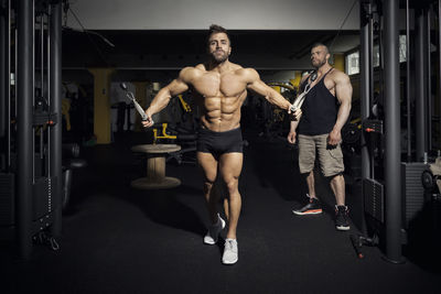 Full length of shirtless man exercising in gym