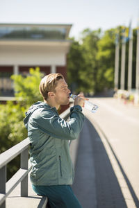 Side view of fit man drinking water on bridge