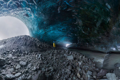 Tourist in outerwear standing near uneven holes in ice surface while exploring cave in vatnajokull glacier on winter day in iceland