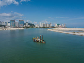 Boats in sea by buildings against blue sky