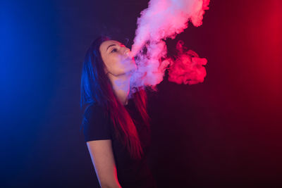 Side view of young woman smoking over black background
