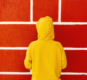 Teenager girl in a yellow sweatshirt or hoodie in a hood against the background of a red wall 