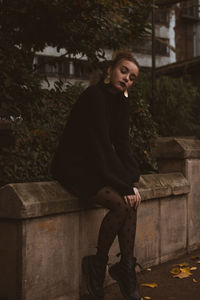 Portrait of young woman sitting on retaining wall