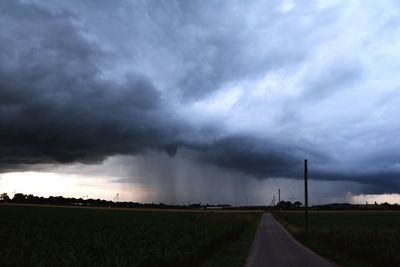 Road on field against storm clouds