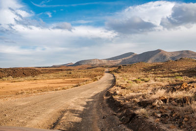 Dirt road leading towards mountains against sky