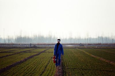 Full length of man holding fire extinguisher while walking on field against sky