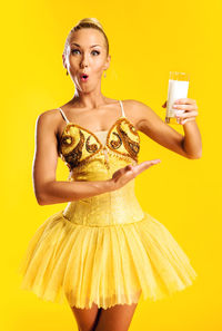 Portrait of surprised beautiful ballerina holding milk glass against yellow background