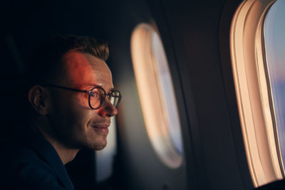 Man with eyeglasses traveling by airplane. passenger looking through window during flight at sunset.