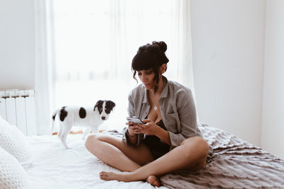 Young woman using mobile phone while sitting on bed at home