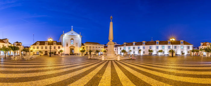 Panoramic view of illuminated buildings in city against blue sky