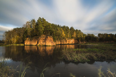 Trees on sandstone formation in river against sky