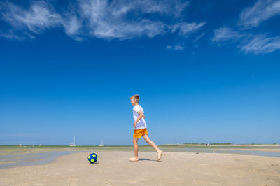 Full length of man standing on beach against blue sky