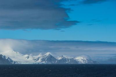 Scenic view of sea and snowcapped mountains against sky