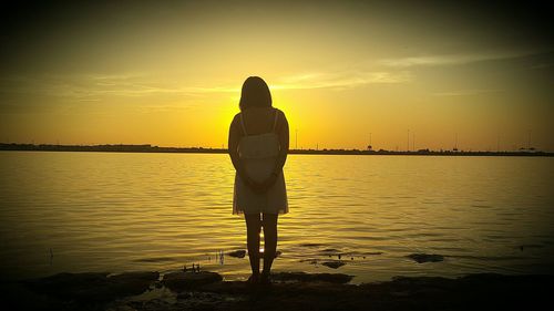 Rear view full length of woman standing at sea shore during sunset