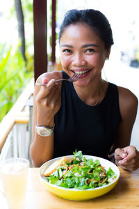 Portrait of happy woman having salad at table in restaurant