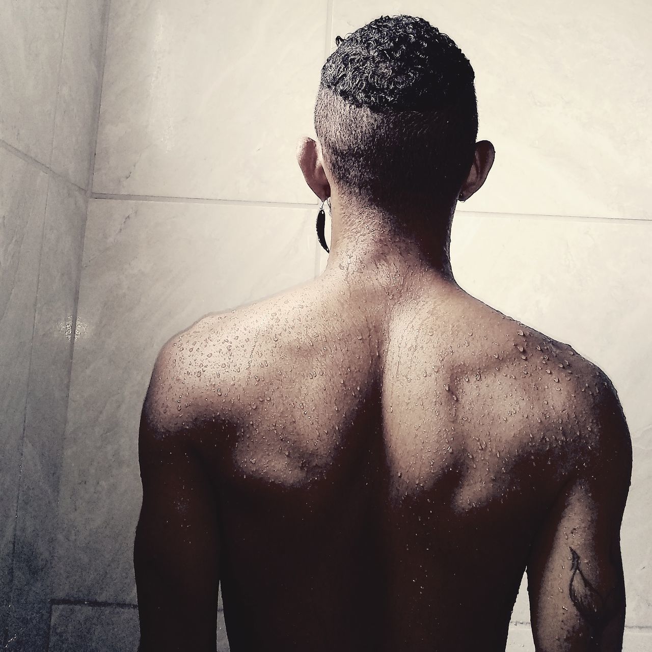 REAR VIEW OF SHIRTLESS MAN STANDING AGAINST WALL IN BATHROOM