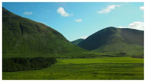 Scenic view of green landscape and mountains against sky