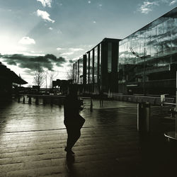 Rear view of woman walking on footpath amidst buildings in city