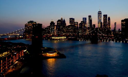 Illuminated buildings by river against sky in city at night