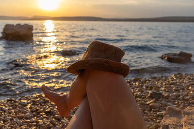 Low section of woman standing at beach against sky during sunset