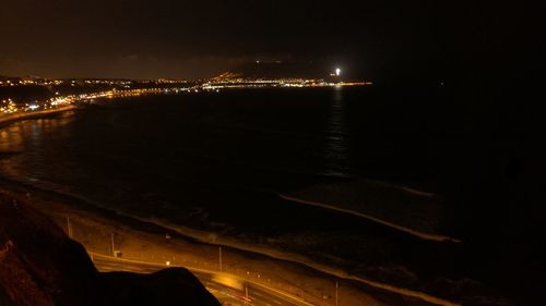 Illuminated city by river against sky at night