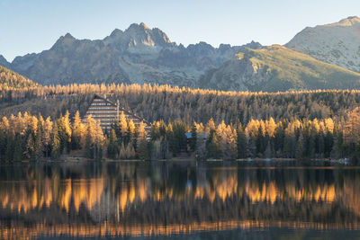 Autumn coloured landscape with a hotel on a bank of a lake with rocky mountains in background