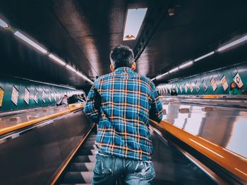 Rear view of man standing on escalator