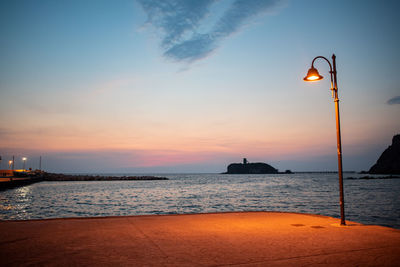 Street light by sea against sky during sunset