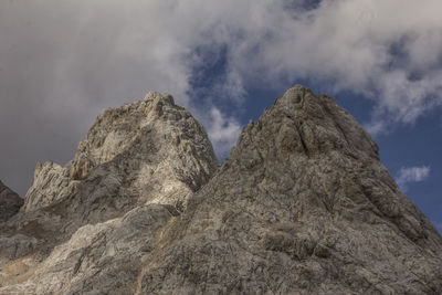 Low angle view of rocky peaks against clouds