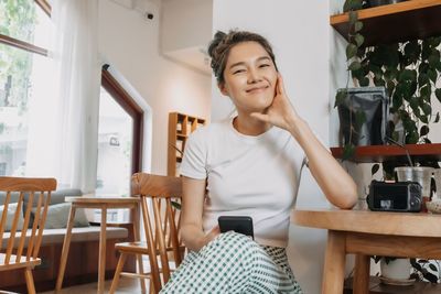 Portrait of young woman using mobile phone while sitting on table
