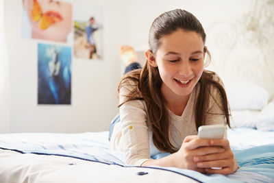 Woman using smart phone lying on bed