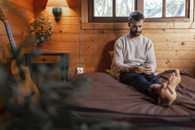 Full length of a young man sitting on bed at home