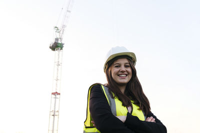 Happy female engineer with arms crossed under clear sky