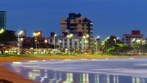 Illuminated buildings by street against sky at night