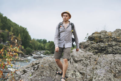 Young man traveler in straw hat with backpack at mountain river