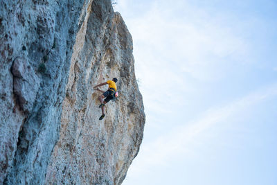 Low angle view of man climbing on rock formation against sky