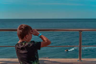 Rear view of boy looking at sea against sky