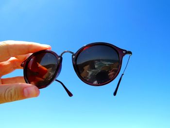 Close-up of hand holding sunglasses against clear blue sky